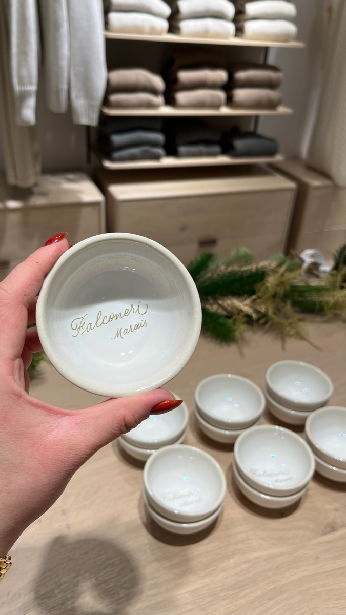 Série de coupelles en céramique gravées à la main et dorées « Falconeri Marais » en lettres cursives, posées en nombre sur une table de boutique