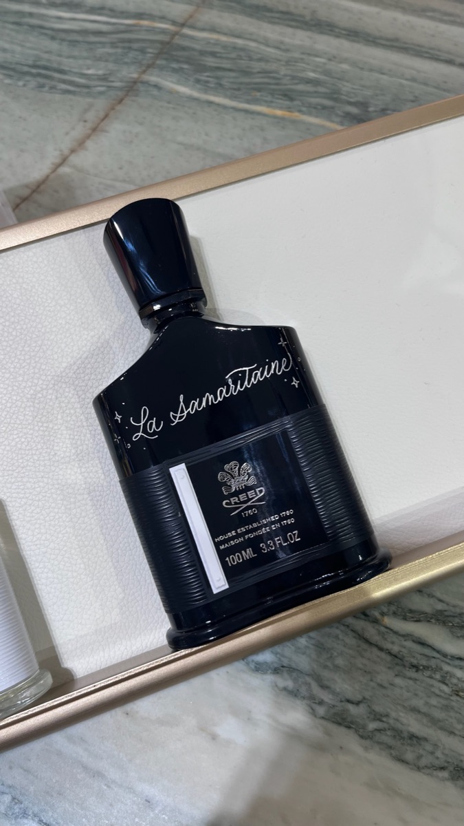 Flacon de parfum noir gravé à la main d'une inscription cursive claire, posé sur un plateau de marbre