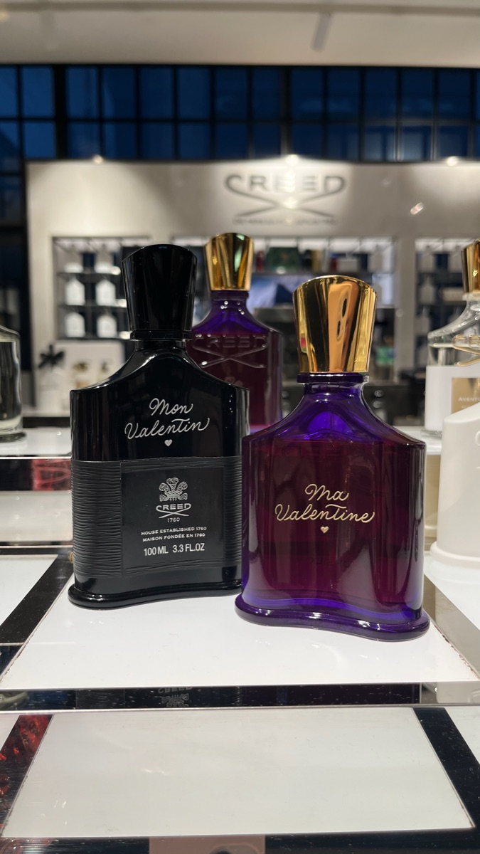 Deux flacons de parfum gravés à la main pour la Saint-Valentin : « Mon Valentin » en doré sur un flacon noir et « Ma Valentine » sur un flacon magenta, chacun avec un petit cœur