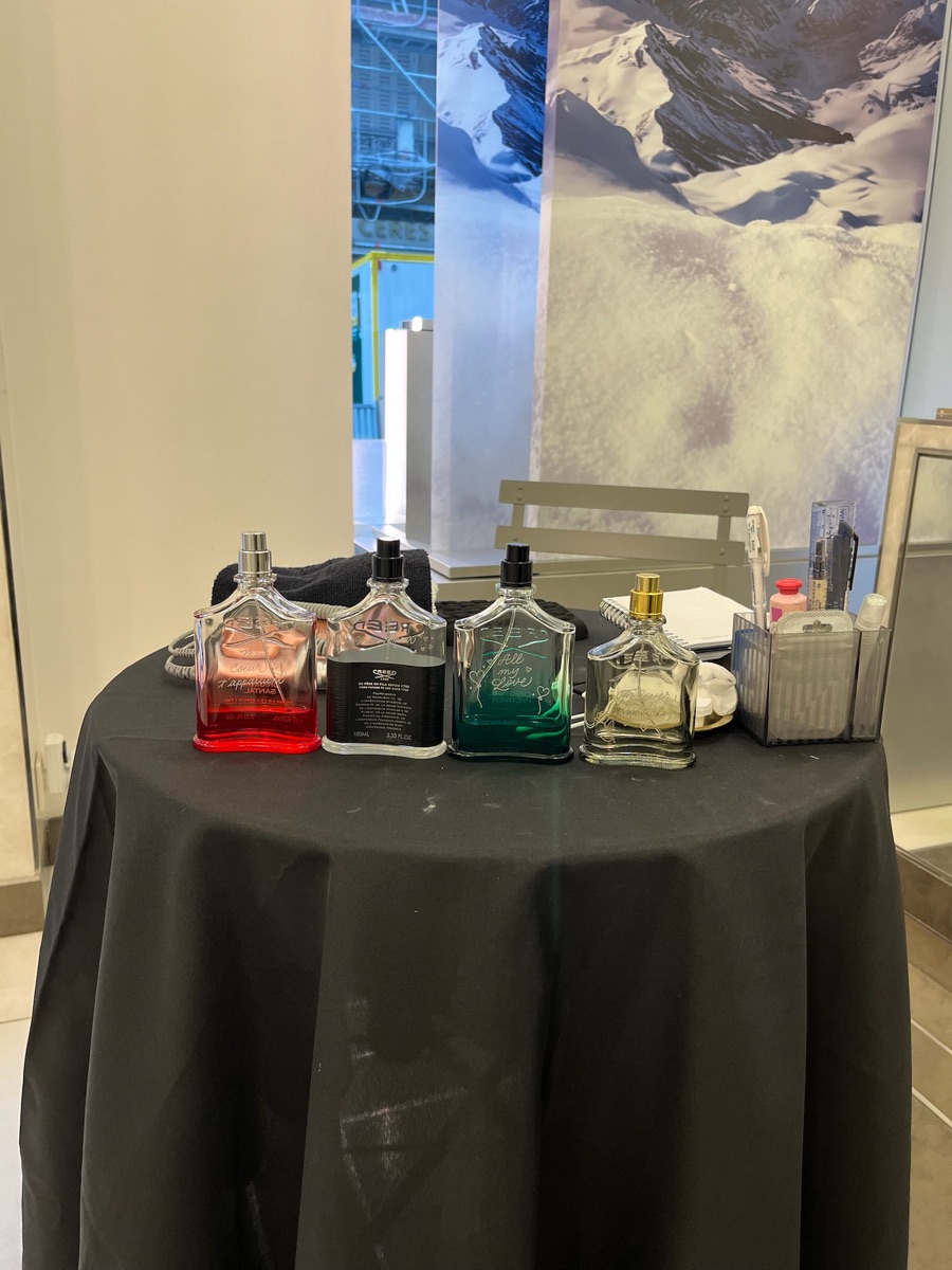 Table d'animation gravure en événement : flacons de parfum Creed gravés au prénom, présentés sur un stand de marque avec décor de montagne