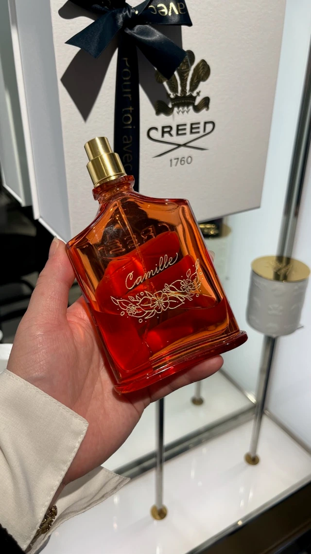 Flacon Creed rouge gravé « Camille » en doré avec un motif floral, devant son coffret