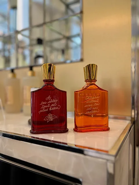Deux flacons Creed rouge et ambré, gravés de dédicaces dorées, sur le comptoir de la boutique
